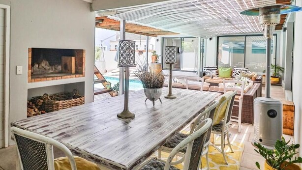 Amplia zona de patio con mesa de madera, sillas de mimbre y vista a la piscina.