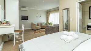 A hotel room with a bed, a desk, a chair, a television, a mirror, and a bathroom. - Hermanus Cliff Path Lodge (Hermanus)