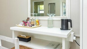 A white console table with a mirror, a tray with various items, a glass bottle, and a black coffee maker. - Hermanus Cliff Path Lodge (Hermanus)