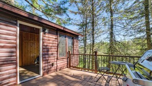 A wooden cabin with a deck, a grill, and a door leading to an interior space. - Hike, Fish & Unwind: Riverfront Vanderbilt Cabin (Vanderbilt)