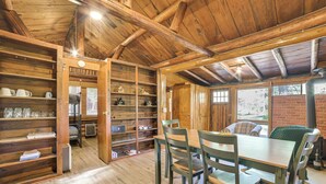 A rustic wooden interior with a dining area, shelves with various items, and a brick wall visible through a window. - Hike, Fish & Unwind: Riverfront Vanderbilt Cabin (Vanderbilt)
