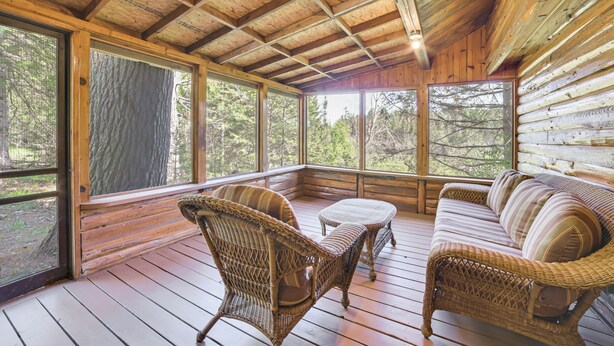 A wooden cabin with a porch, wicker furniture, and large windows. - Hike, Fish & Unwind: Riverfront Vanderbilt Cabin (Vanderbilt)