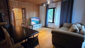Una sala de estar con piso de madera, un sofá, un televisor y un comedor con una mesa y sillas.