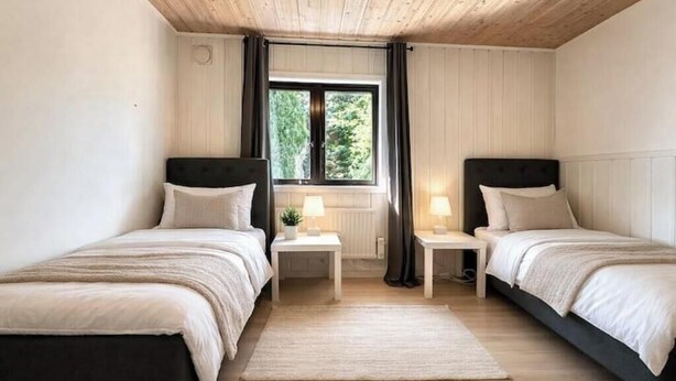 Un dormitorio con dos camas, una ventana con cortinas, un radiador y una mesita de noche con lámpara.