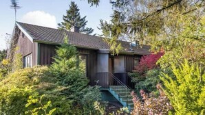 Una casa moderna con techo inclinado, rodeada de abundante follaje y árboles.