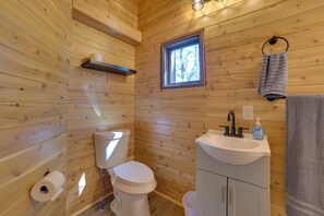 A wooden cabin bathroom with a toilet, sink, and window.