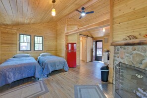 Uma cabana de madeira com duas camas, um refrigerador vermelho, uma lareira de pedra e um ventilador de teto.