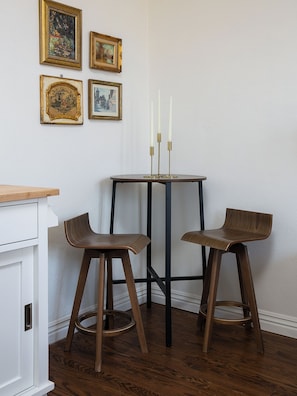A corner room with a dining table, two stools, and three framed pictures on the wall.