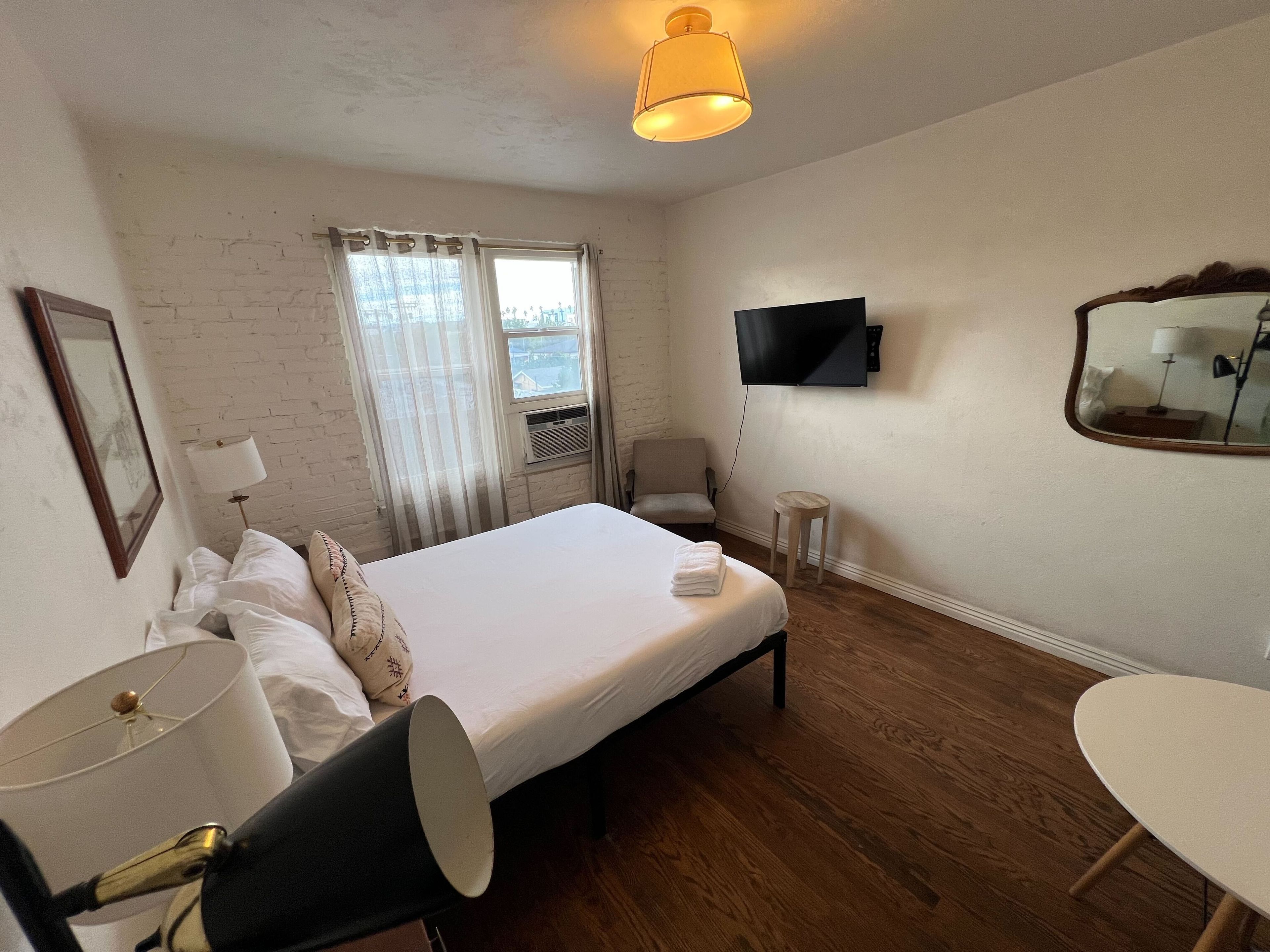 A hotel room with a bed, a TV, a desk, a chair, a lamp, and a window with curtains.