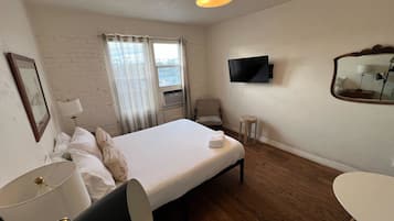 A hotel room with a bed, a TV, a desk, a chair, a lamp, and a window with curtains.