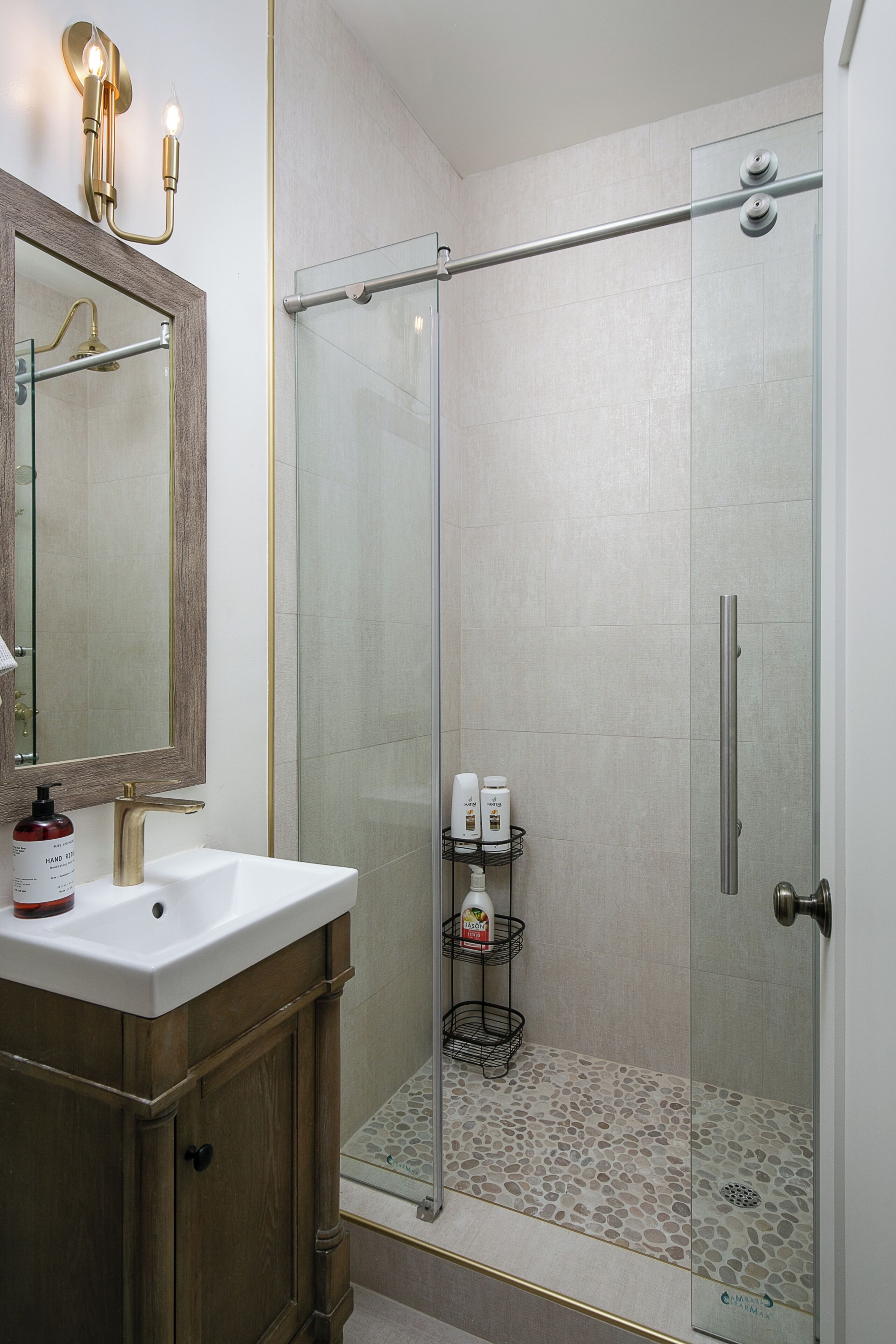 Un baño moderno con cabina de ducha de vidrio, tocador de madera y espejo con luces empotradas.