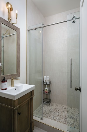 A modern bathroom with a glass shower enclosure, a wooden vanity, and a mirror with wall-mounted lights.