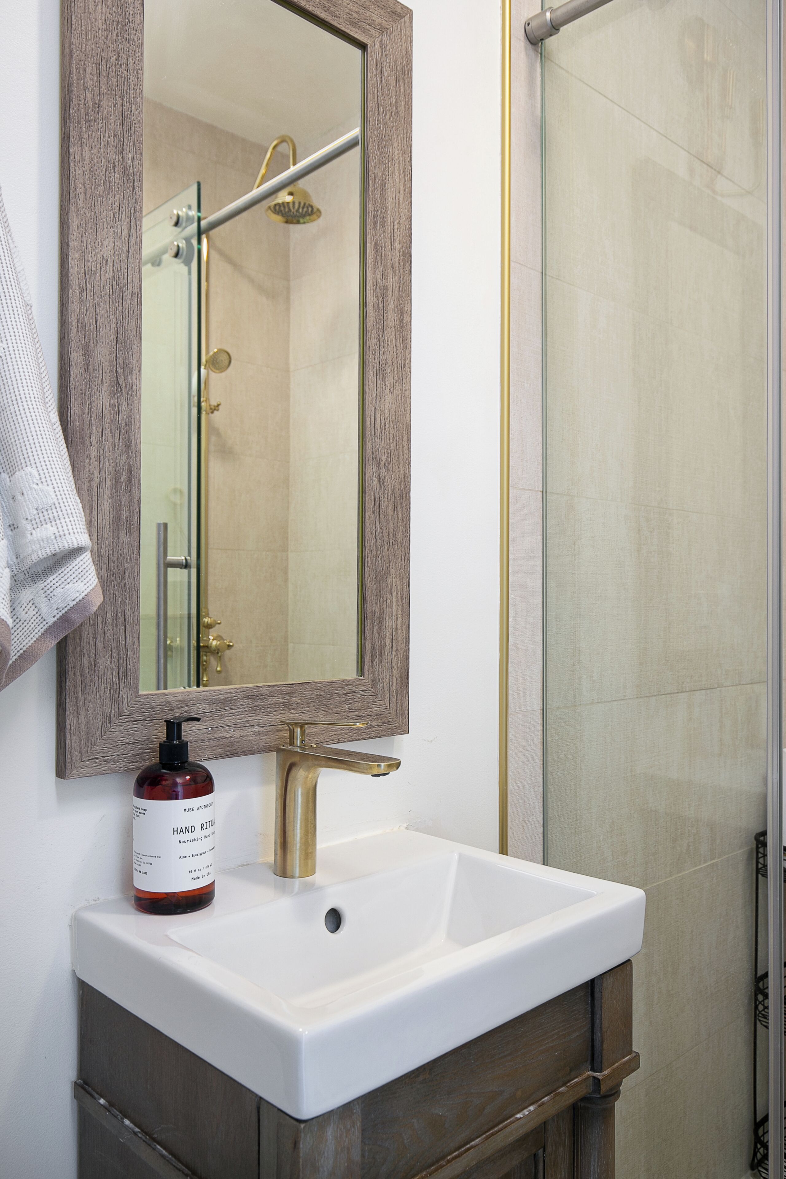 A bathroom with a white sink, a wooden vanity, a mirror with a wooden frame, and a shower area.