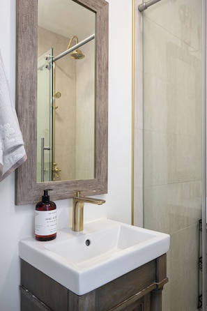 A bathroom with a white sink, a wooden vanity, a mirror with a wooden frame, and a shower area.