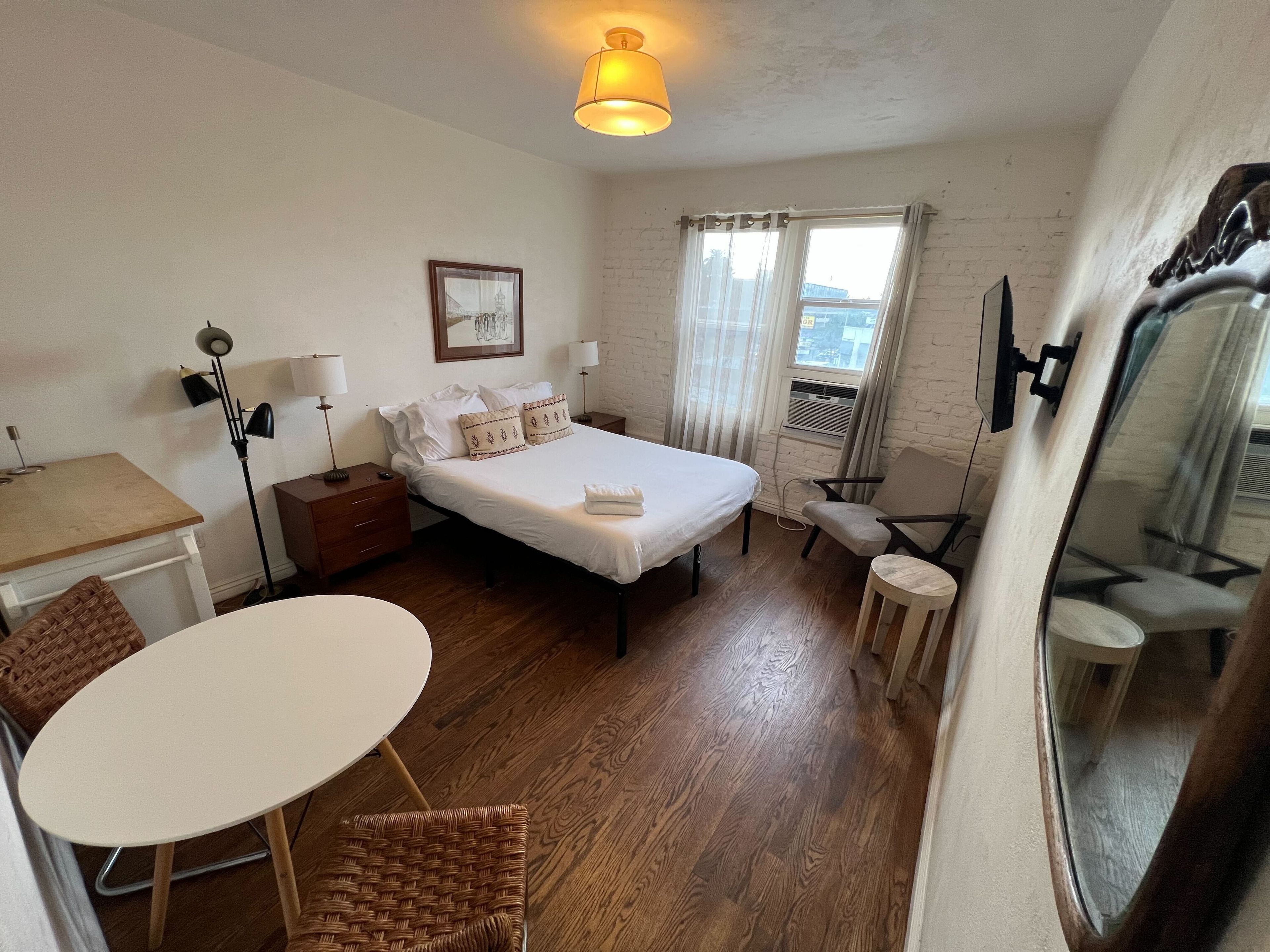 Een kleine hotelkamer met een bed, nachtkastjes, een bureau, een stoel en een klein rond tafeltje.