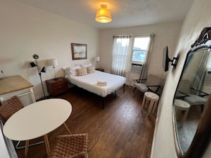 A compact hotel room with a bed, bedside tables, a desk, a chair, and a small round table.