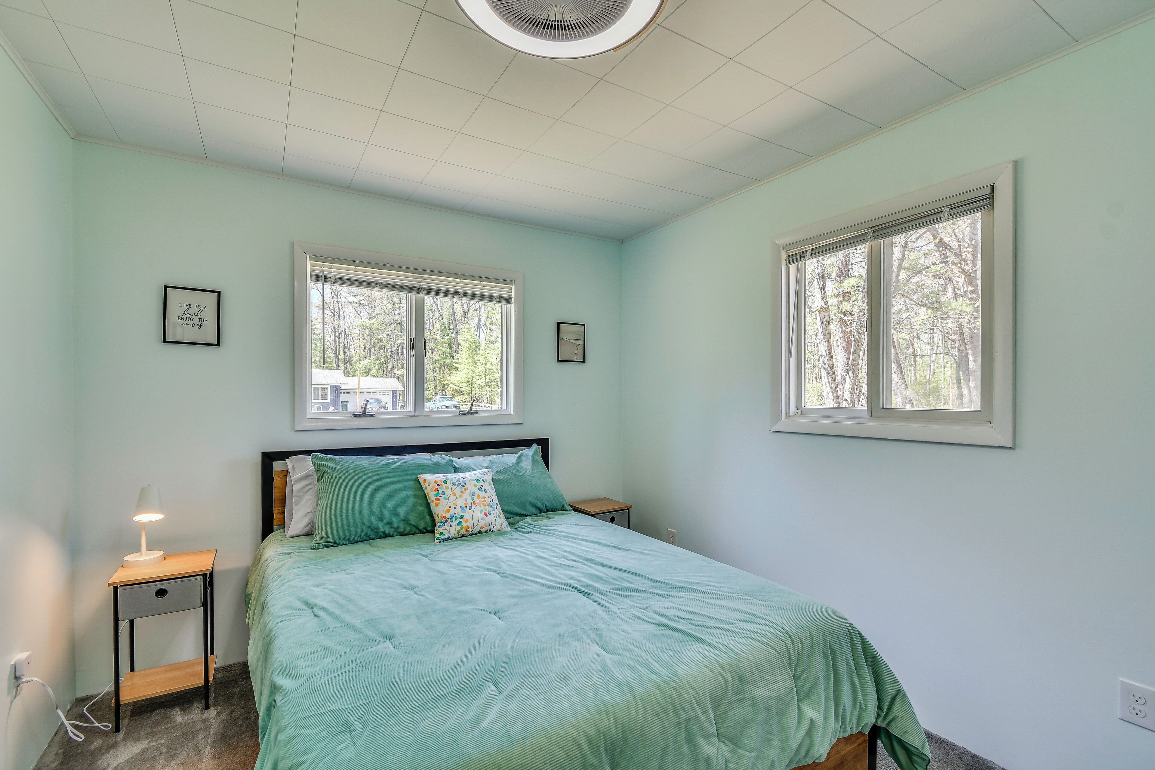 Une chambre à coucher comprenant un lit, deux tables de chevet, une commode, une fenêtre et un ventilateur de plafond.
