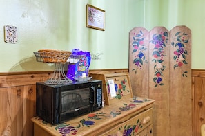 A microwave on a wooden counter with a basket, a bag of chips, and a framed picture.