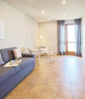 A modern living room with a blue sofa, white chairs, a lamp, and a large window with curtains. - The Seven Ways - Maple Apartment with Jacuzzi and Large Porch (Piemonte)