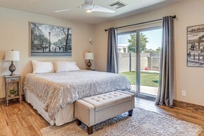 Ein Schlafzimmer mit einem großen Bett, einer Bank, einem Deckenventilator und Blick ins Freie durch eine Schiebetür.
