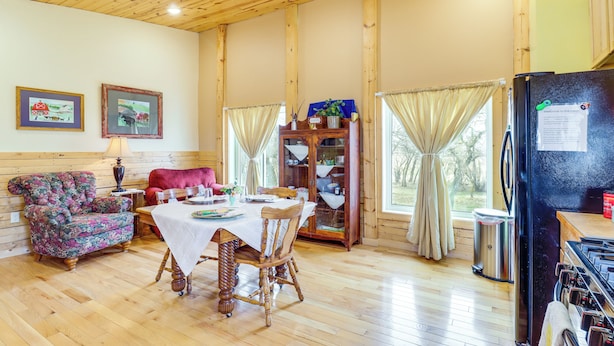 A wooden-paneled room with a dining table, chairs, a sofa, a cabinet, and a refrigerator. - Peaceful Prairie Living! Rural Willow City Apt (Willow City)