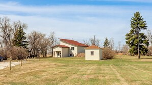 A two-story house with a red roof, a small attached garage, and a fenced yard. - Peaceful Prairie Living! Rural Willow City Apt (Willow City)