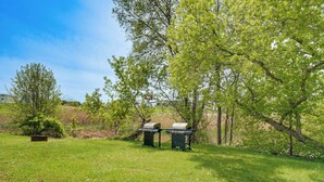 A grassy area with two barbecue grills and a bench.