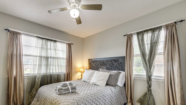 A bedroom with a bed, curtains, a ceiling fan, and a nightstand with a lamp. - Spacious Yard! Family Home, 10 Mi to Fort Bragg (Fayetteville)