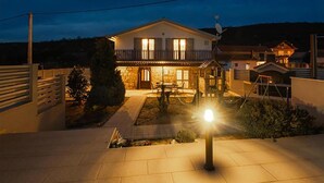 A two-story house with a balcony, a satellite dish, and a well-lit front yard at night. - Gorgeous home in Trilj (Trilj)