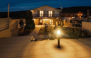 Ein zweistöckiges Haus mit Balkon, Satellitenschüssel und beleuchtetem Vorgarten bei Nacht.
