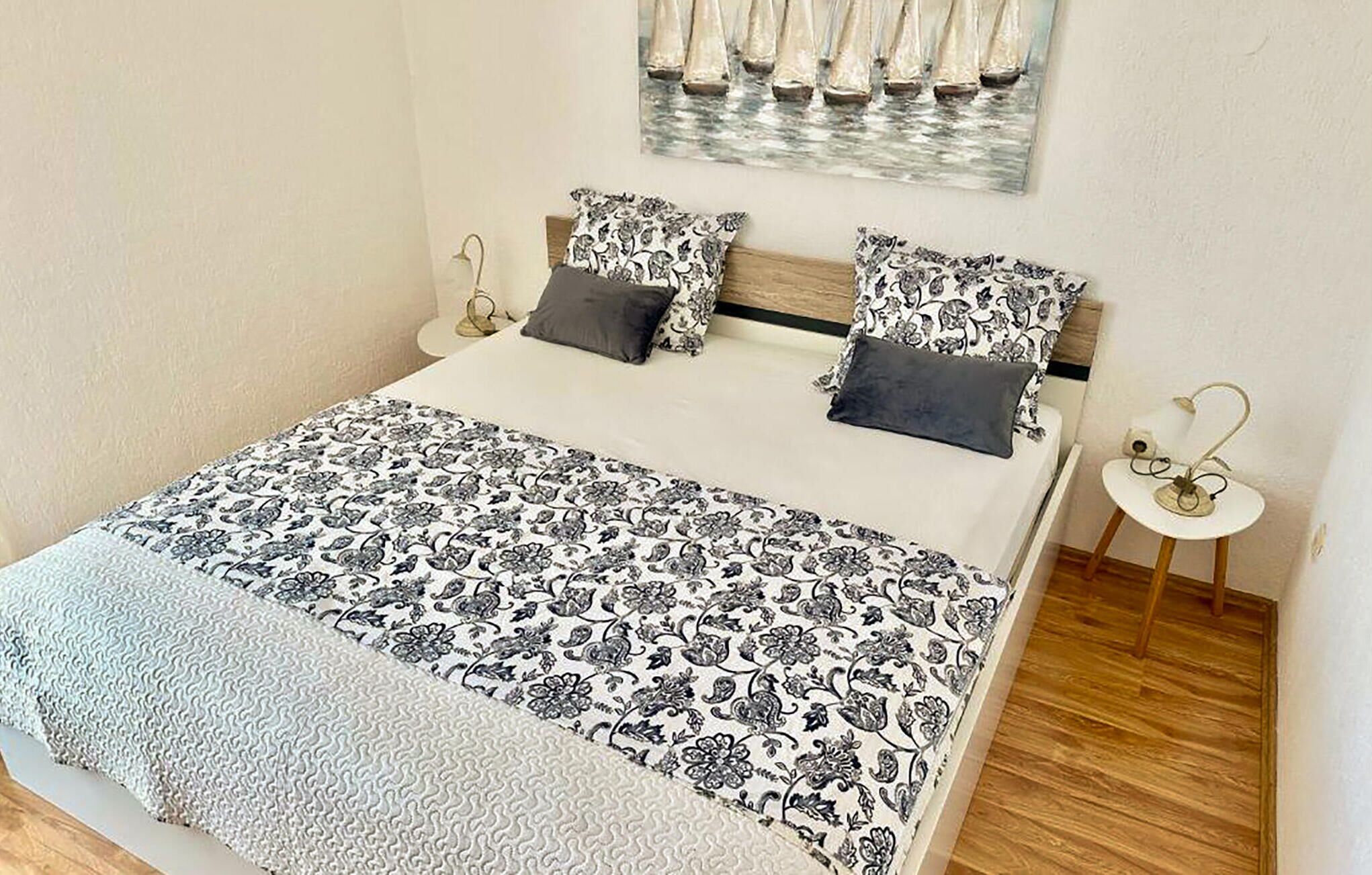Een opgemaakt bed met beddengoed met een patroon, een klein nachtkastje met een lamp, en een kunstwerk aan de muur.