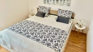 A neatly made bed with patterned bedding, a small bedside table with a lamp, and a wall-mounted artwork. - Gorgeous home in Trilj (Trilj)
