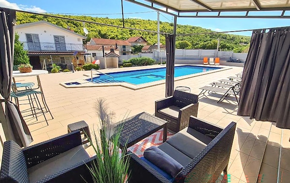 Ein Poolbereich mit Gartenmöbeln, einem Schwimmbad und einer Aussicht auf Häuser im Hintergrund.