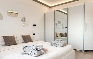 Ein modernes Schlafzimmer mit Bett, Kissen, einem großen Spiegel und einem Kleiderschrank.