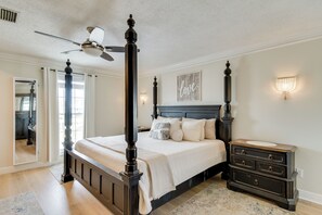 A bedroom with a four-poster bed, a nightstand, a dresser, a ceiling fan, and a wall-mounted light fixture. - Unwind Poolside, Walk to Beach! Gulf Shores Escape (Gulf Shores)