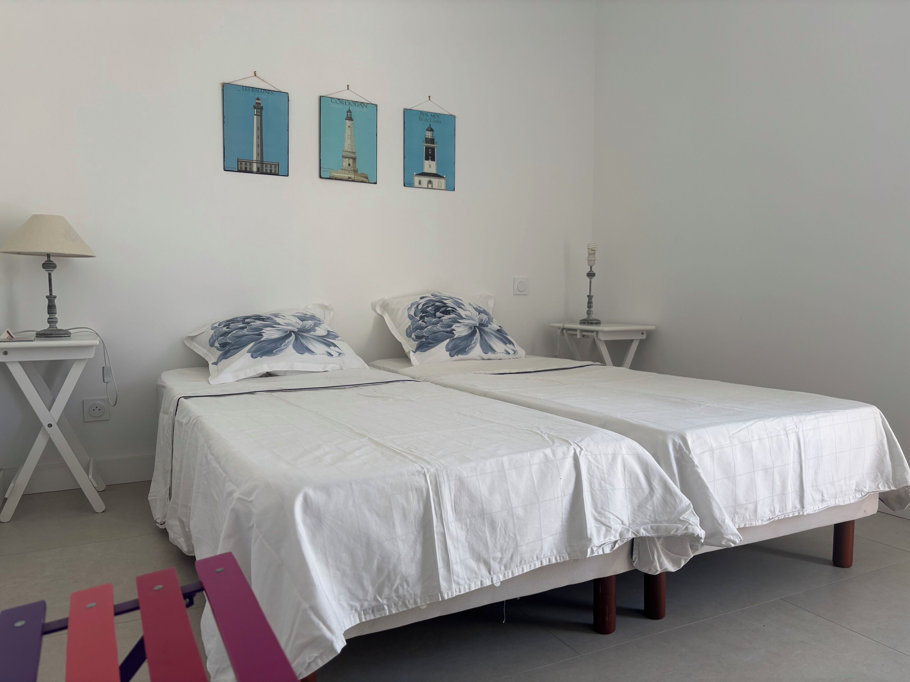Una camera da letto con due letti, un comodino con una lampada, un tavolino con una candela e tre quadri appesi al muro.