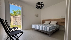 A bedroom with a bed, a chair, a hanging light fixture, and a view of the outdoors. - Escapade rochelaise: new, modern house (La Rochelle)