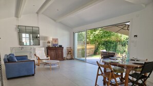 A spacious living area with a dining table, chairs, a sofa, and a large sliding glass door leading to a garden. - Escapade rochelaise: new, modern house (La Rochelle)