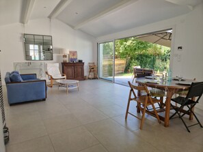 Ein geräumiges Wohnzimmer mit Esstisch, Stühlen, einer Couch und einer großen Schiebeglasdoor, die zu einem Garten führt.