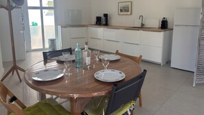 A dining area with a round table set for four, a kitchen in the background, and a sliding glass door leading to an outdoor area. - Escapade rochelaise: new, modern house (La Rochelle)