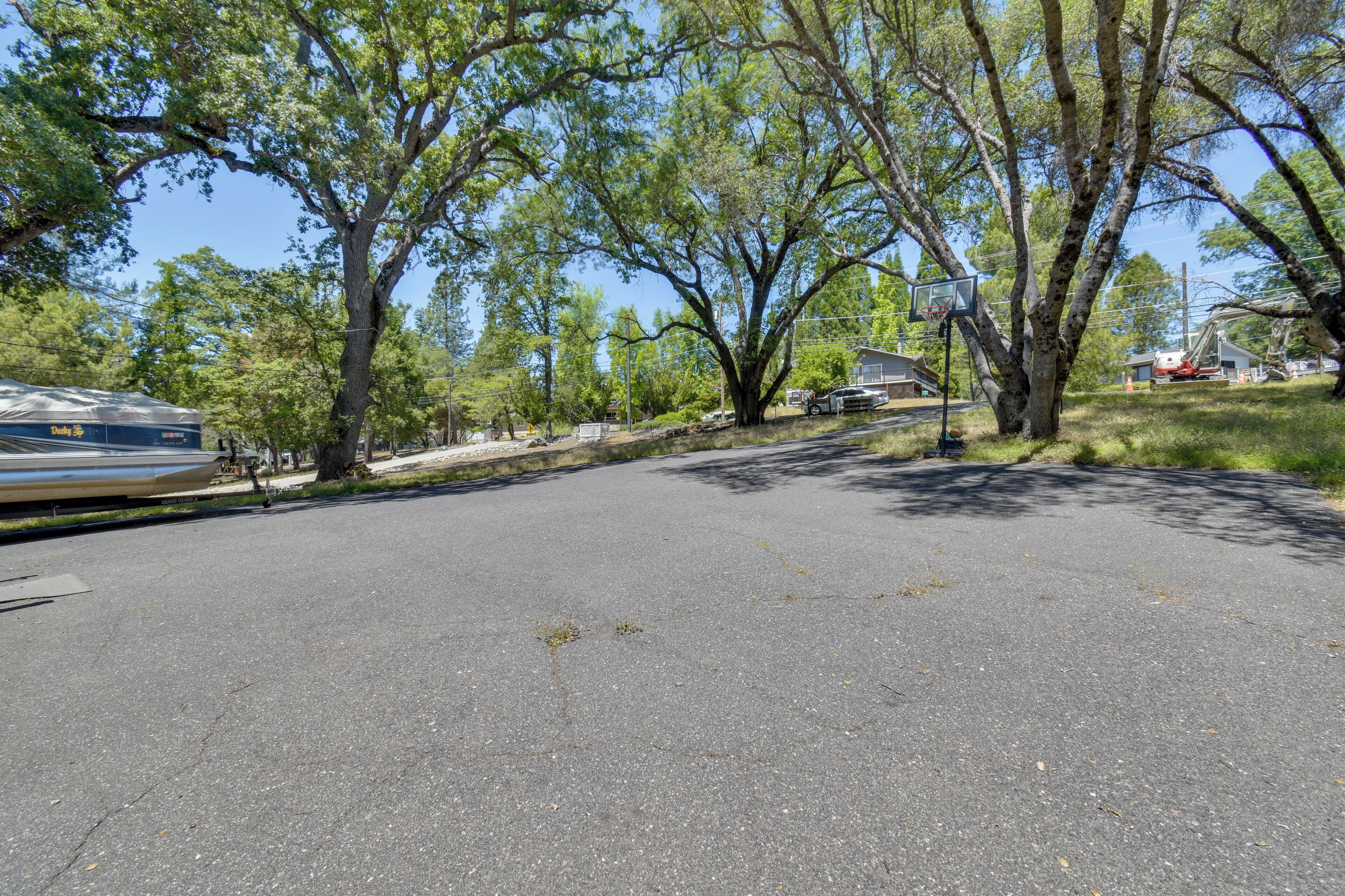 A paved area with trees, a basketball hoop, and a parked vehicle.