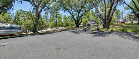 A paved area with trees, a basketball hoop, and a parked vehicle.