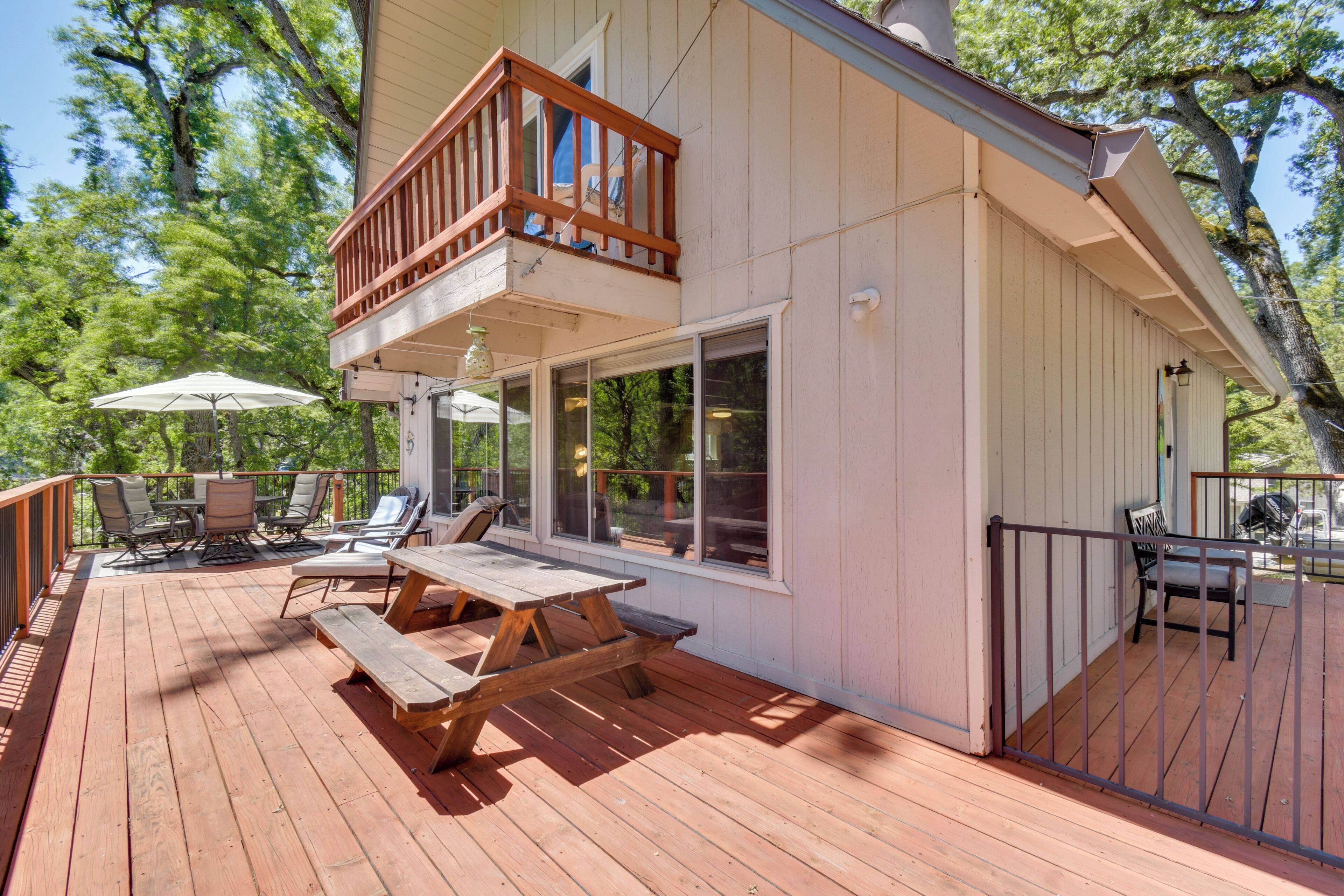 A wooden deck with a picnic table and chairs, a covered seating area, and a balcony with a railing.