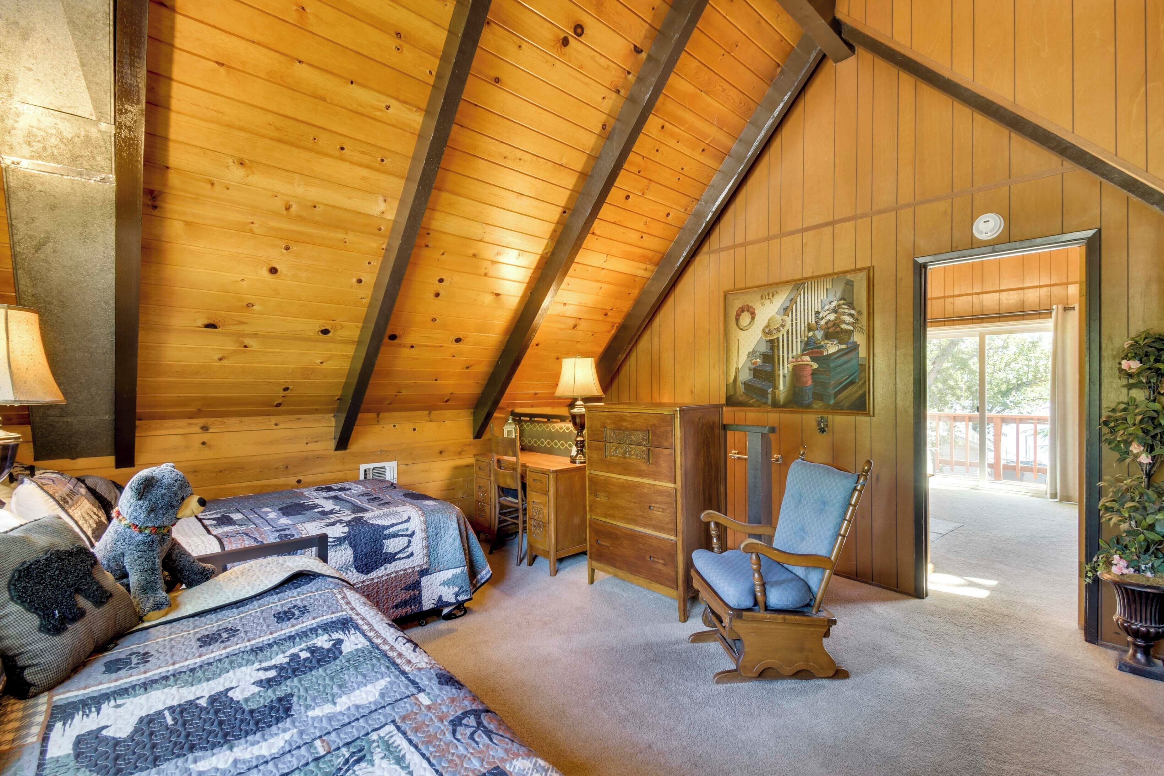 A cozy room with a sloped ceiling, wooden walls, a desk, a chair, and a bed with a quilt.