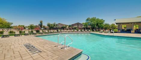 A clear blue swimming pool with a brick deck, lounge chairs, and a covered seating area.