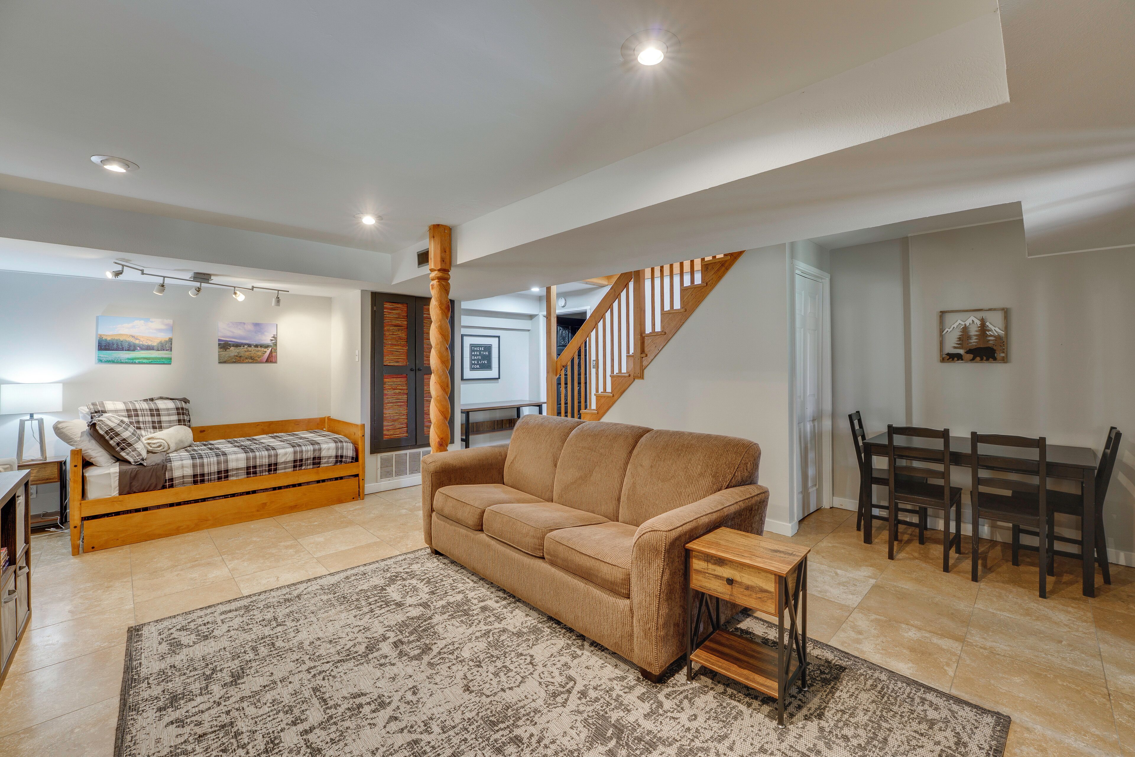 A living room with a sofa, a dining table with chairs, a staircase, and artwork on the walls.