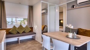 Habitación compacta con un banco, una mesa, sillas, una orquídea en maceta y un aire acondicionado de pared.