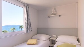 Habitación pequeña con cama individual, ventana con vistas panorámicas, mesita de noche y estante con un adorno.