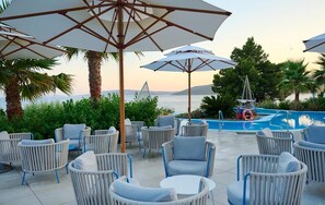 Sitzgelegenheiten im Freien mit Sonnenschirmen, einem Pool und Meerblick.
