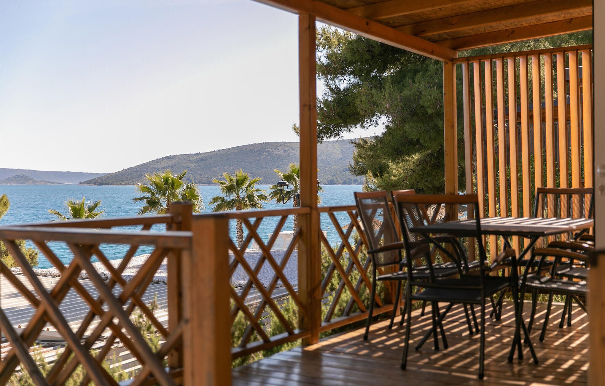 A wooden deck with a table and chairs overlooking a body of water and hills.